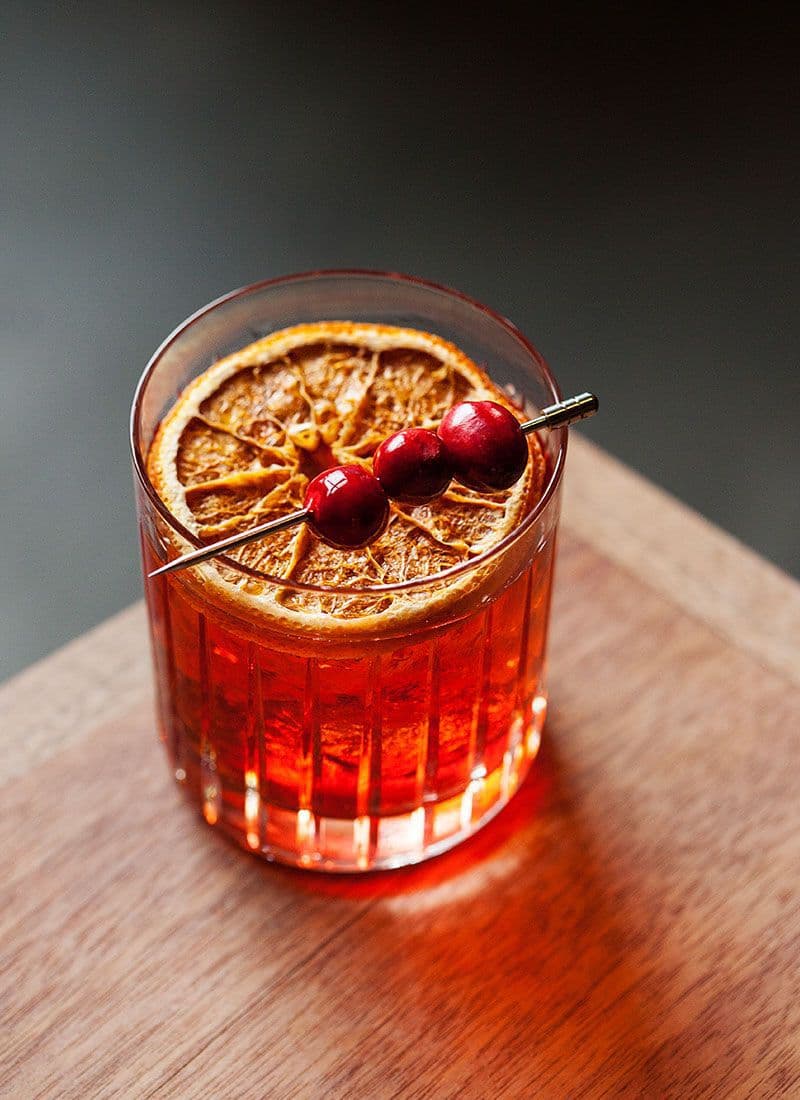 Red cocktail with a dried orange slice and cherry on a wooden surface